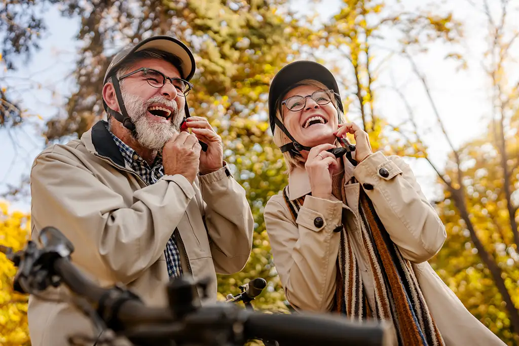 A senior couple smiling in parka jackets while adjusting their helmets to go bike riding.