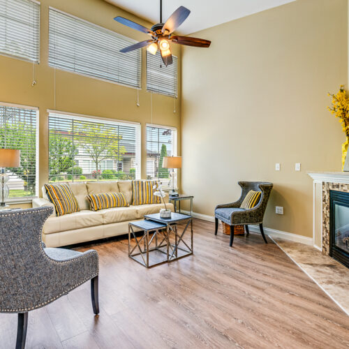 Cottage living room with couch and chairs lit by natural lighting from the large windows